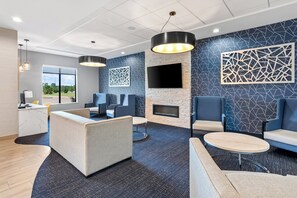 A modern waiting area with seating, a fireplace, and a large TV screen.