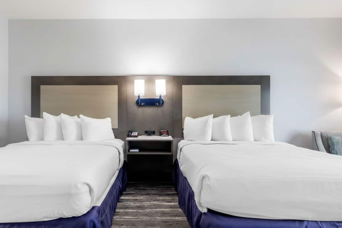 Une chambre d’hôtel avec deux lits, une table de chevet, un luminaire fixé au mur et un tableau encadré accroché au mur.