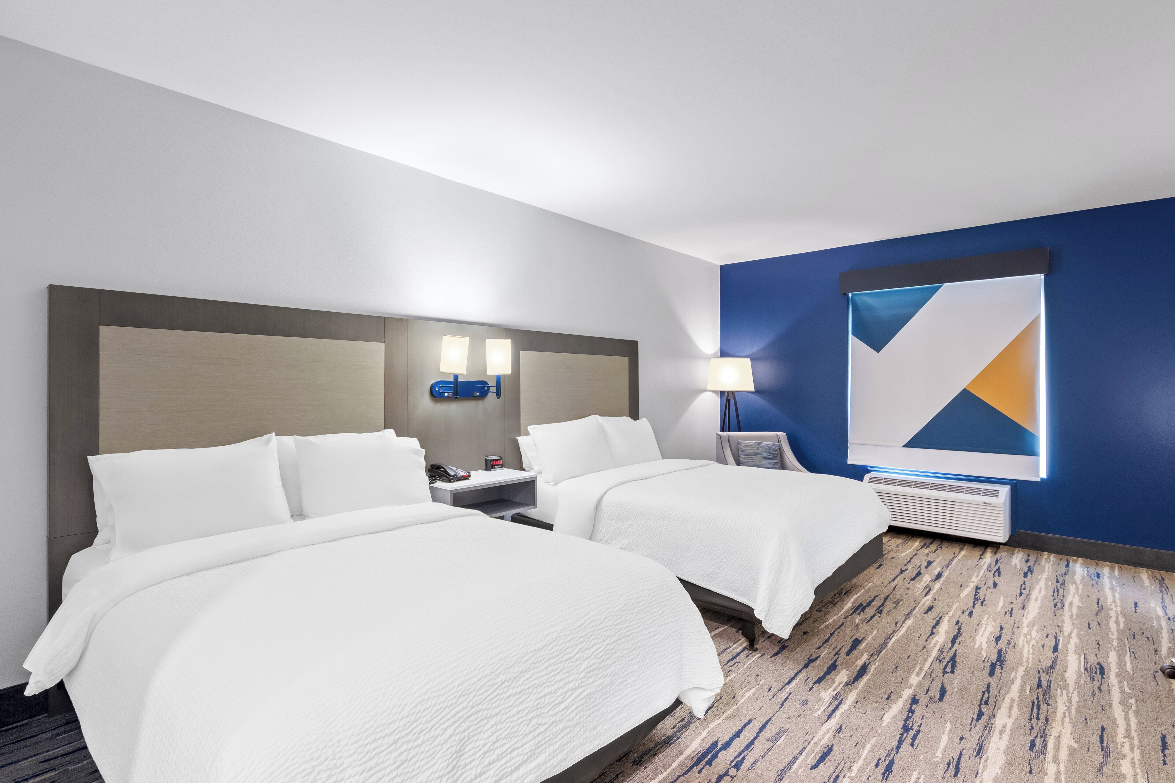 A hotel room with two beds, a nightstand with a lamp, a wall clock, and a large abstract painting.