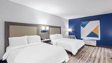 A hotel room with two beds, a nightstand with a lamp, a wall clock, and a large abstract painting.