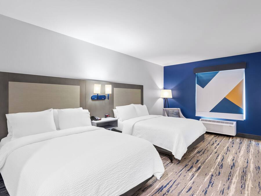 A hotel room with two beds, a nightstand with a lamp, a wall clock, and a large abstract painting.