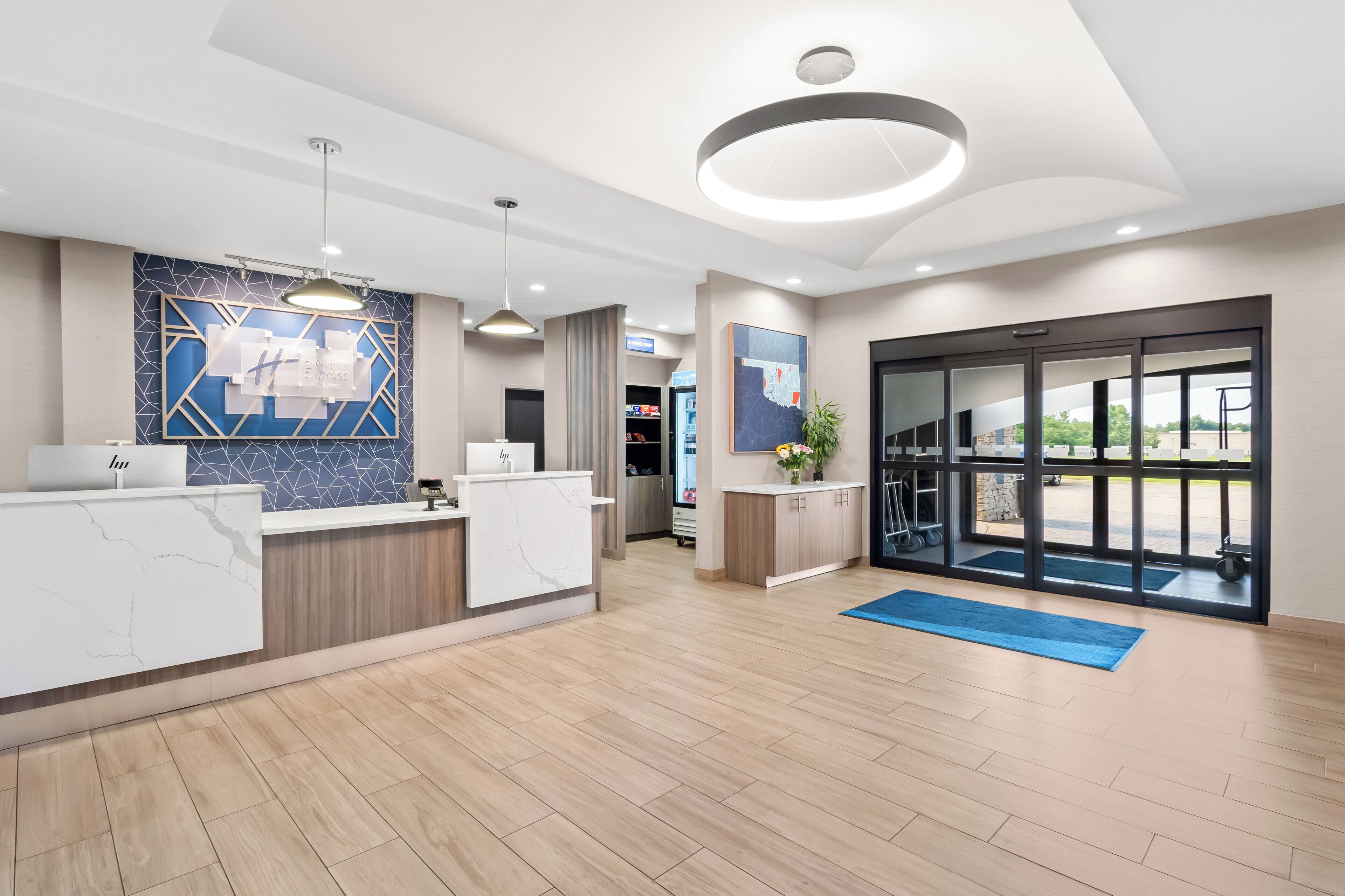A hotel reception area with a marble counter, a blue geometric wall design, a large window with a view, and a modern ceiling light fixture.