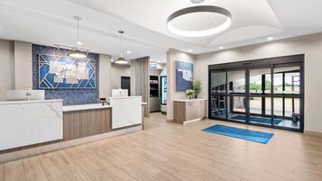 A hotel reception area with a marble counter, a blue geometric wall design, a large window with a view, and a modern ceiling light fixture.