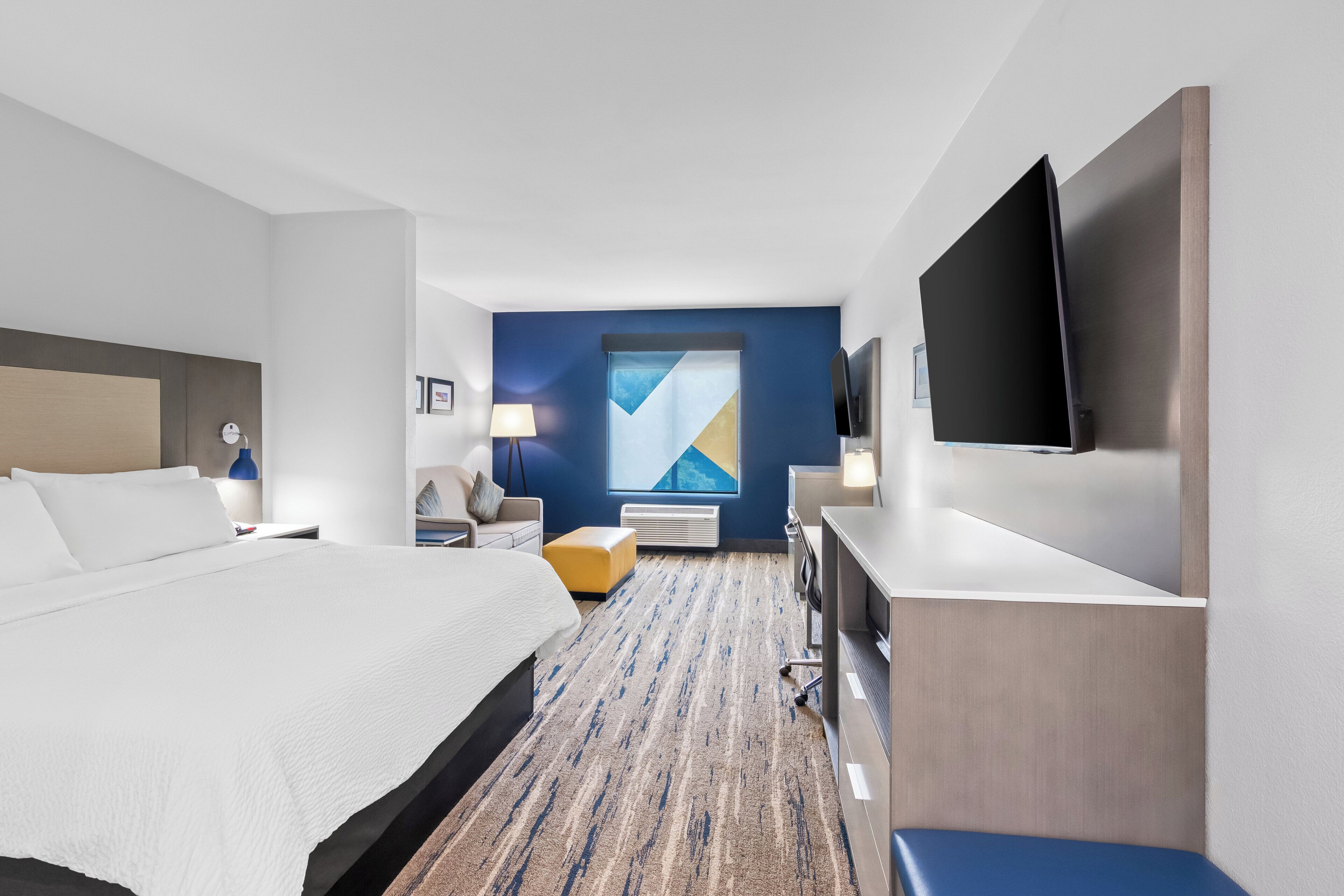 A hotel room with a large bed, a desk, a chair, a flat-screen TV, and a window with a view.