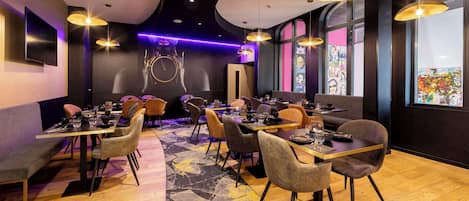 A modern restaurant with multiple dining tables and chairs, ambient lighting, and large windows.