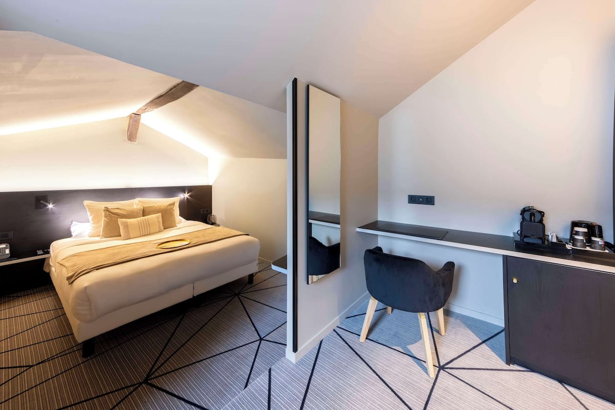 A modern hotel room with a bed, bedside table, and a small desk area with a chair.