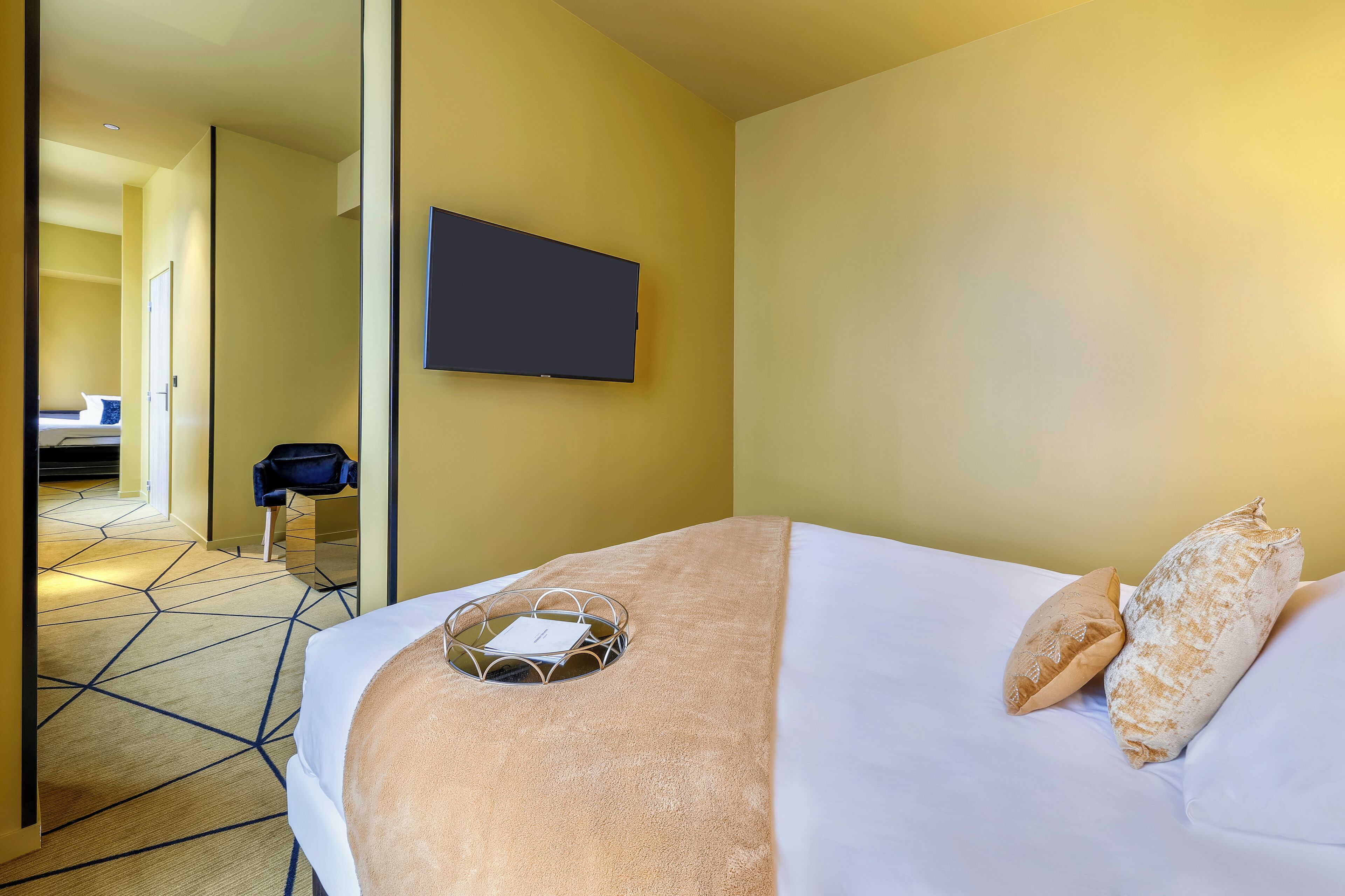 A hotel room with a bed, a TV mounted on the wall, and a mirror reflecting the room.