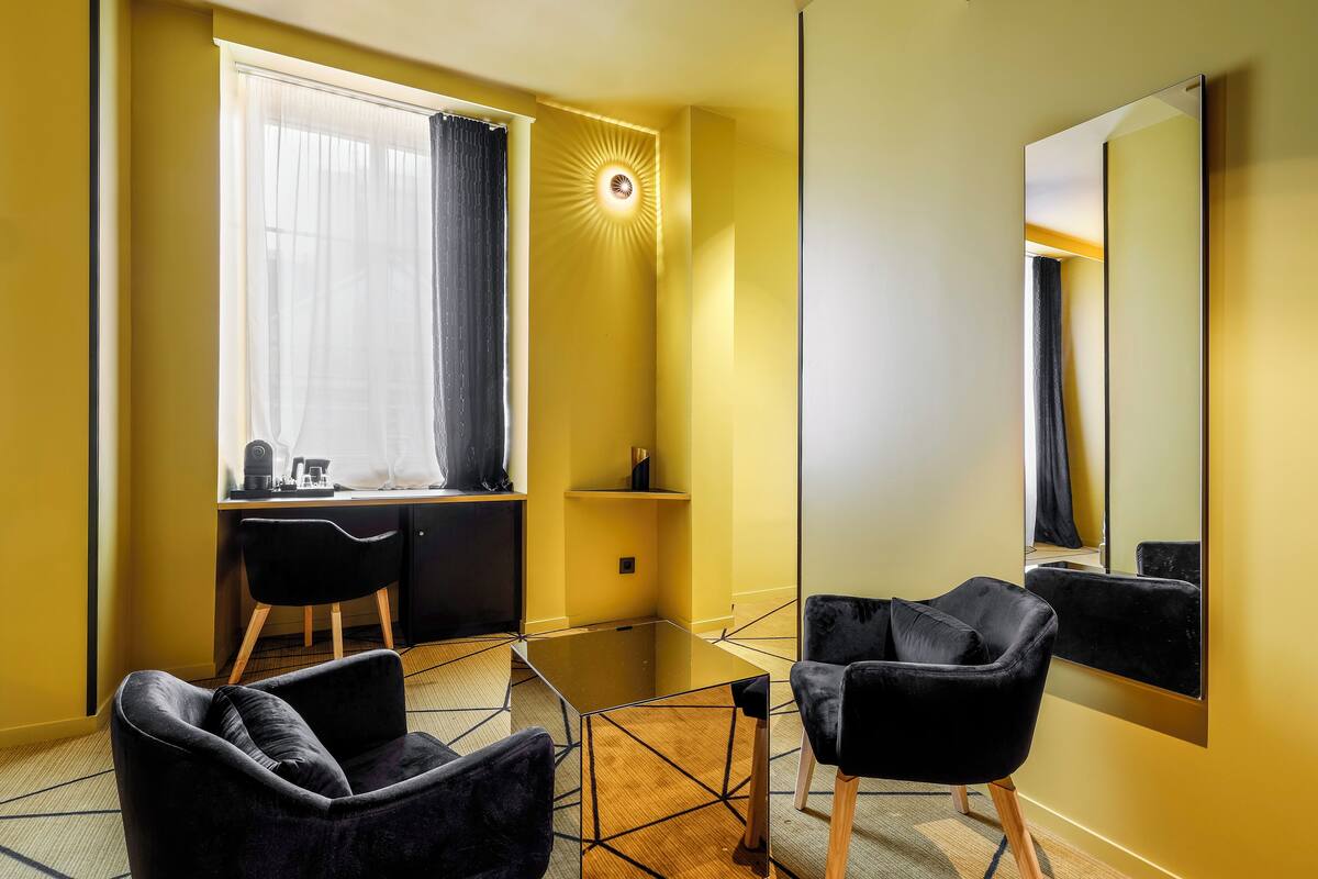 A modern room with a glass table, two black chairs, a desk with a computer, and a large mirror on the wall.