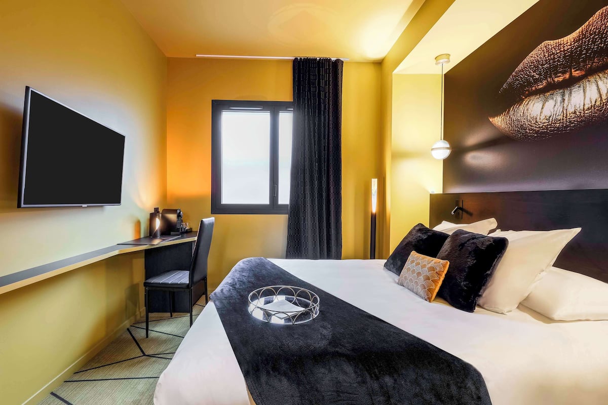 A hotel room with a bed, a desk, a chair, a TV, and a window with curtains.