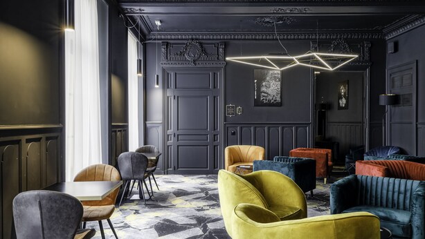 A modern interior with a geometric patterned carpet, a variety of upholstered chairs in different colors, and a unique geometric light fixture. - Leprince Hotel Spa, BW Premier Collection (Le Mans)