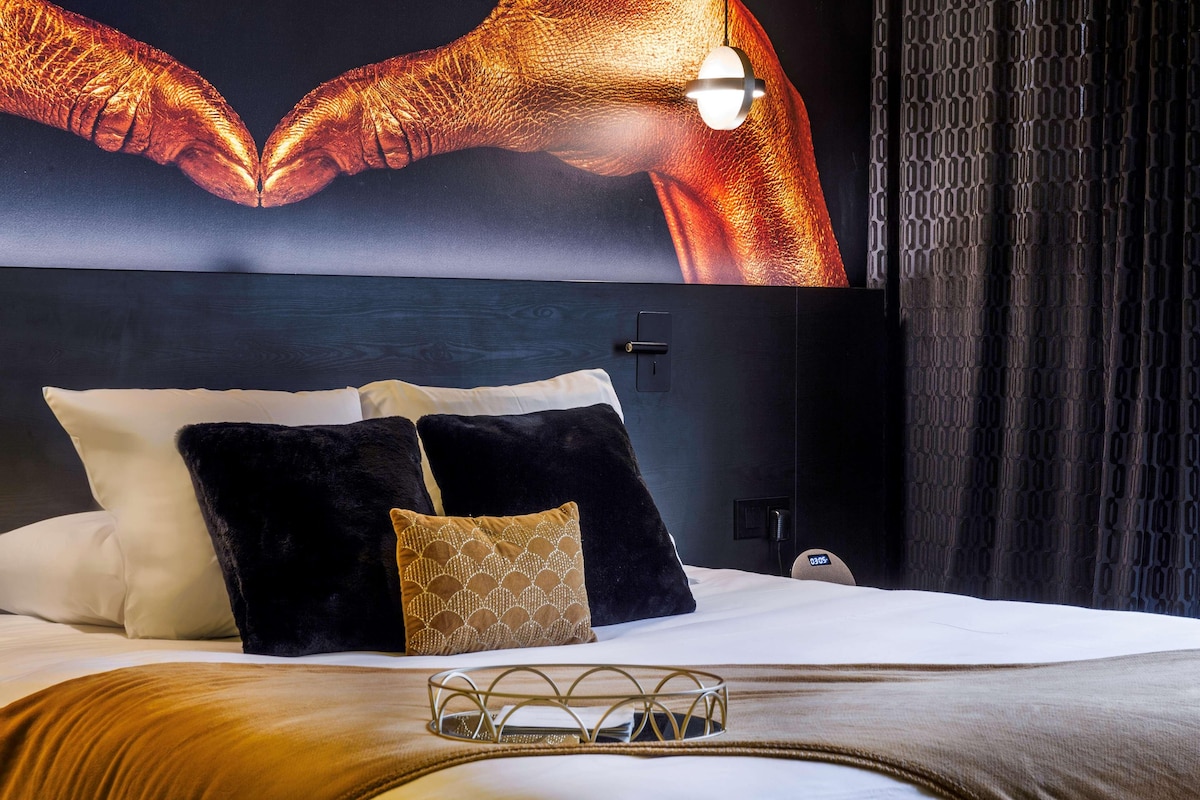 A hotel room with a large bed, a headboard with a poster, and a nightstand with a lamp.
