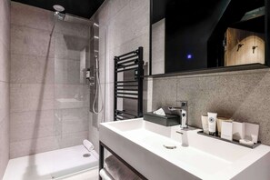 Un baño moderno con ducha de vidrio, lavamanos blanco y espejo grande.