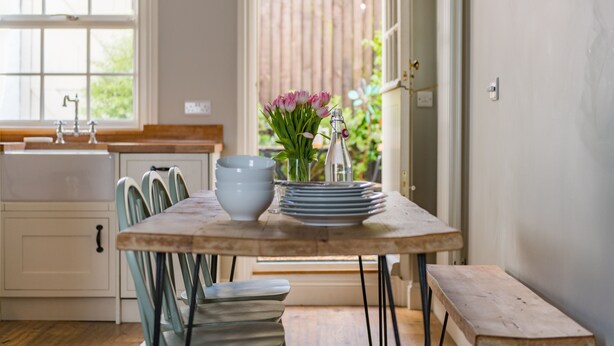 A kitchen with a wooden table, chairs, a sink, and a window with curtains.