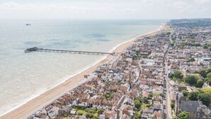 An aerial view of a coastal town with a beach, a pier, and a dense cluster of buildings.