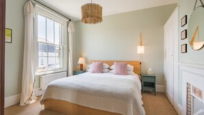 A neatly arranged bedroom with a large bed, bedside lamps, and a hanging light fixture. - Fig Tree House, Deal, Kent (Deal)