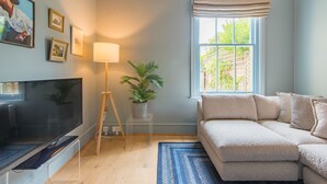 A living room with a flat-screen TV, a lamp, a potted plant, a sofa, and a window with a view of greenery. - Fig Tree House, Deal, Kent (Deal)