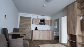A modern kitchen with wooden cabinets, a microwave, and a coffee maker. There is a dining area with a table and chairs. - Smart & Stay Aparthotel (Saarlouis)