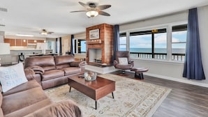 A spacious living room with a fireplace, leather sofas, and a large window overlooking the ocean. - La Anahi - Oceanfront Vacation Rental (St. Augustine)