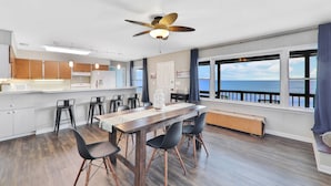A modern kitchen with a central island, a dining area with a wooden table and chairs, and large windows offering a view of the sea. - La Anahi - Oceanfront Vacation Rental (St. Augustine)