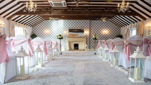 A venue with a long aisle flanked by tables with white tablecloths and pink sashes, a fireplace, and chandeliers. - Batch Country House (Weston-super-Mare)