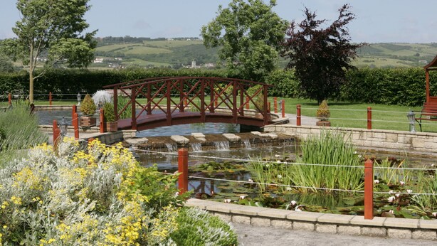 A garden with a bridge, a pond, and surrounding greenery. - Batch Country House (Weston-super-Mare)