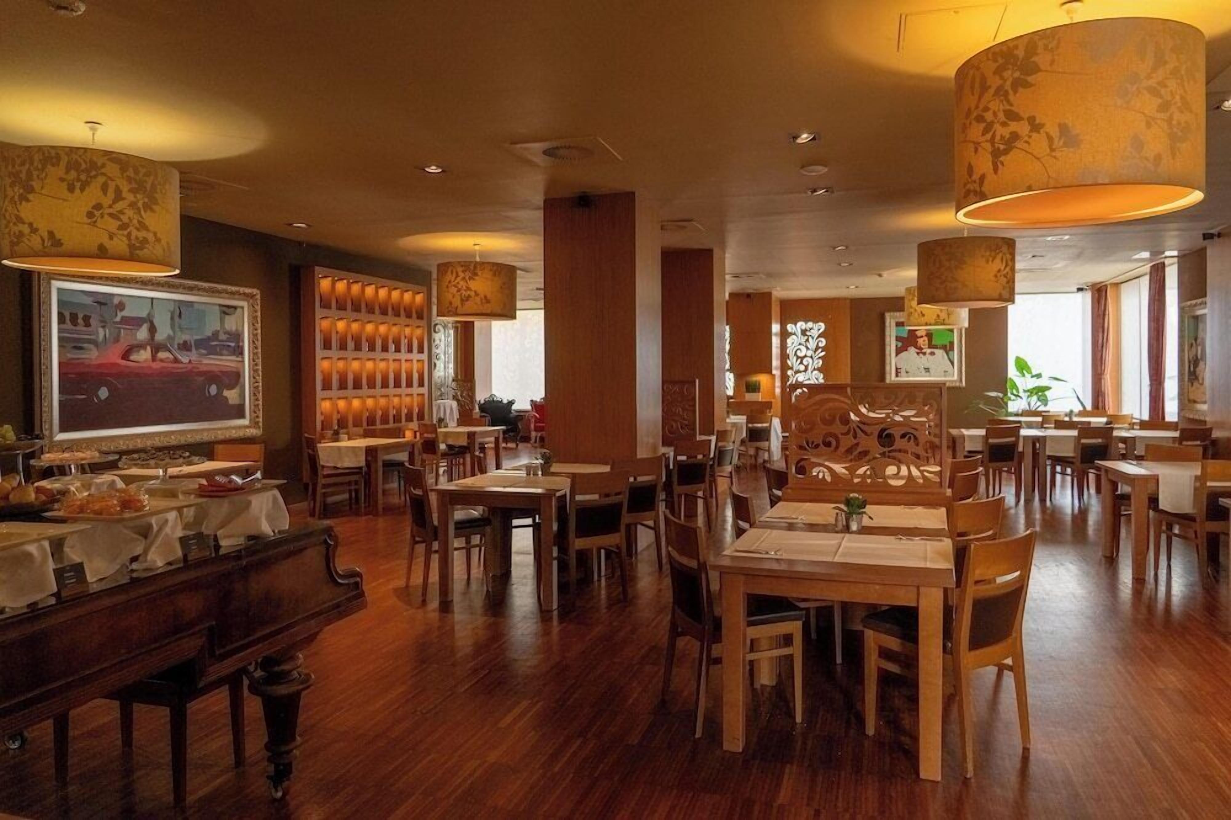 A restaurant with wooden tables and chairs, hanging lamps, and framed artwork on the walls.