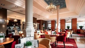 A hotel lobby with round tables, red and beige chairs, a chandelier, and a red carpet. - Hotel Evropa Celje (Celje)