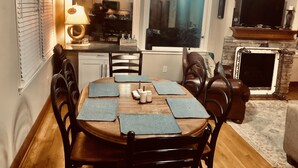 A dining area with a wooden table, black chairs, and blue placemats. There is a kitchen visible through an open door, a fireplace, and a television mounted above it. - Chalet Suzanne of Helen (Helen)