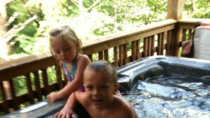 Two children in a hot tub with a wooden deck and greenery in the background. - Chalet Suzanne of Helen (Helen)