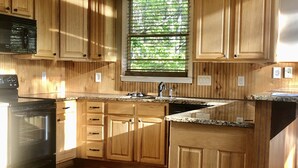 A kitchen with wooden cabinets, a built-in microwave, a stove, and a window with blinds. - Chalet Suzanne of Helen (Helen)