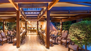 An outdoor dining area with multiple tables and chairs, a bar in the background, and a covered walkway. - Villa Sonia by Estia Adults Only (Hersonissos)