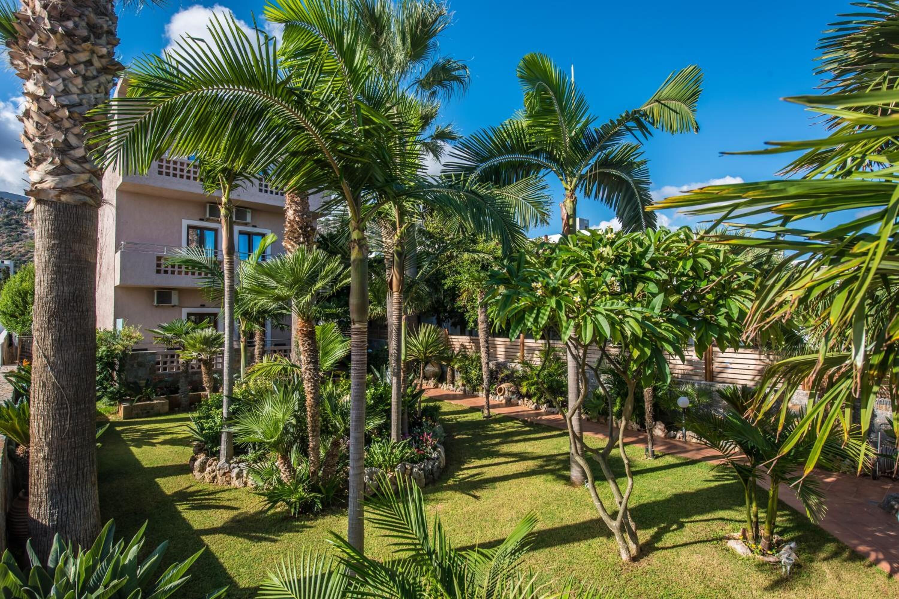 A lush garden with palm trees and a building with balconies.