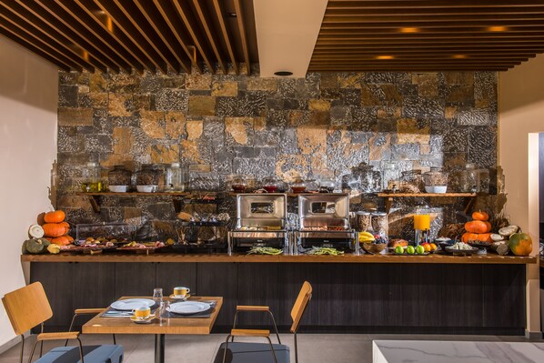 A breakfast bar with stone backsplash, buffet with food and drinks, and seating area with chairs and tables.