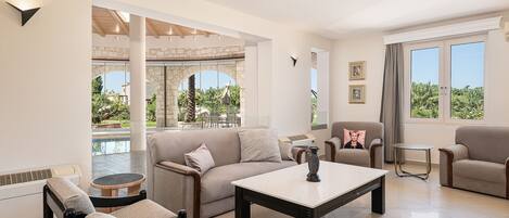 A modern living room with a sofa, chairs, a coffee table, and a view of an outdoor pool area.