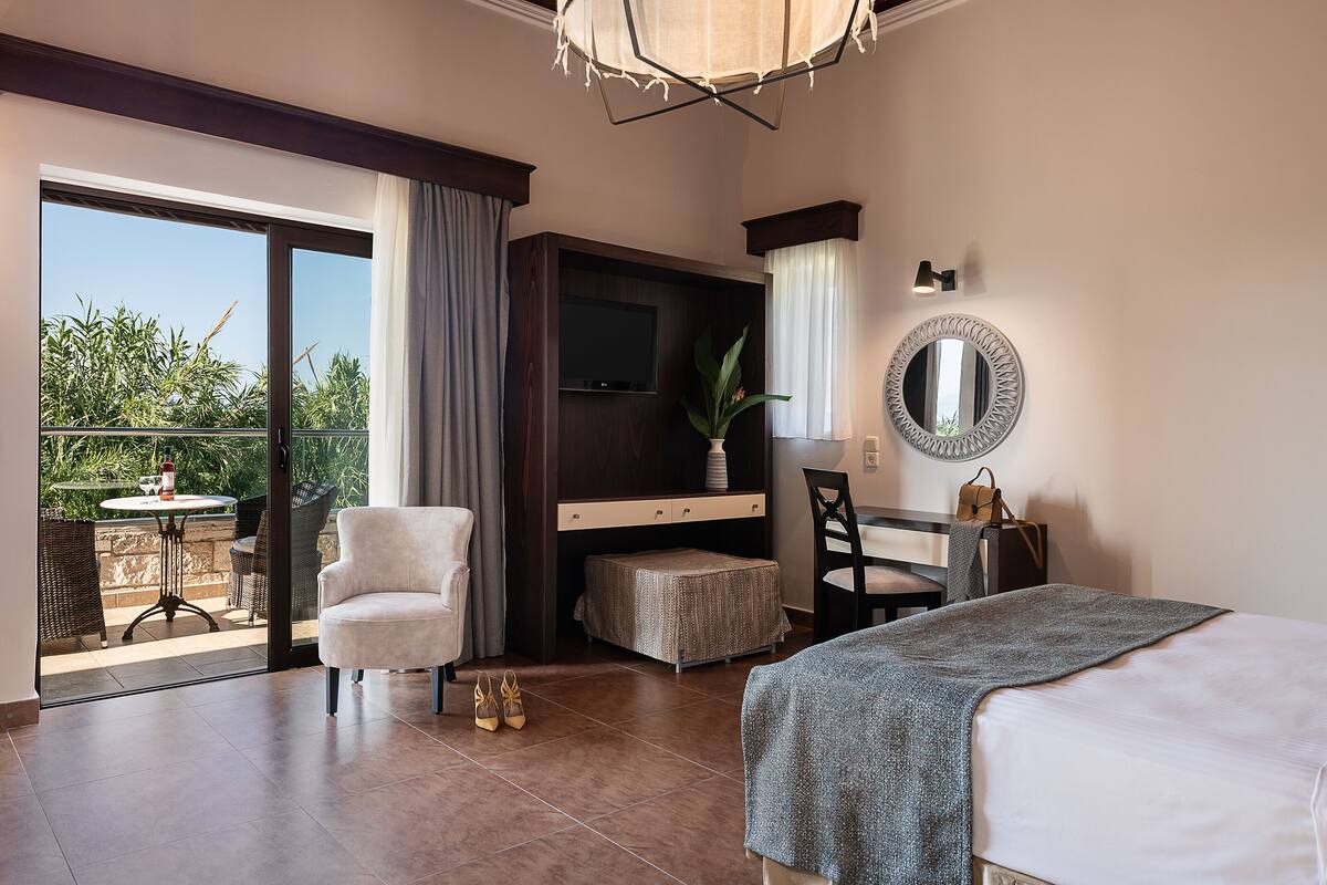 Ein Hotelzimmer mit Bett, Schreibtisch, Stuhl, kleinem Tisch und einem Balkon mit Tisch und Stühlen.