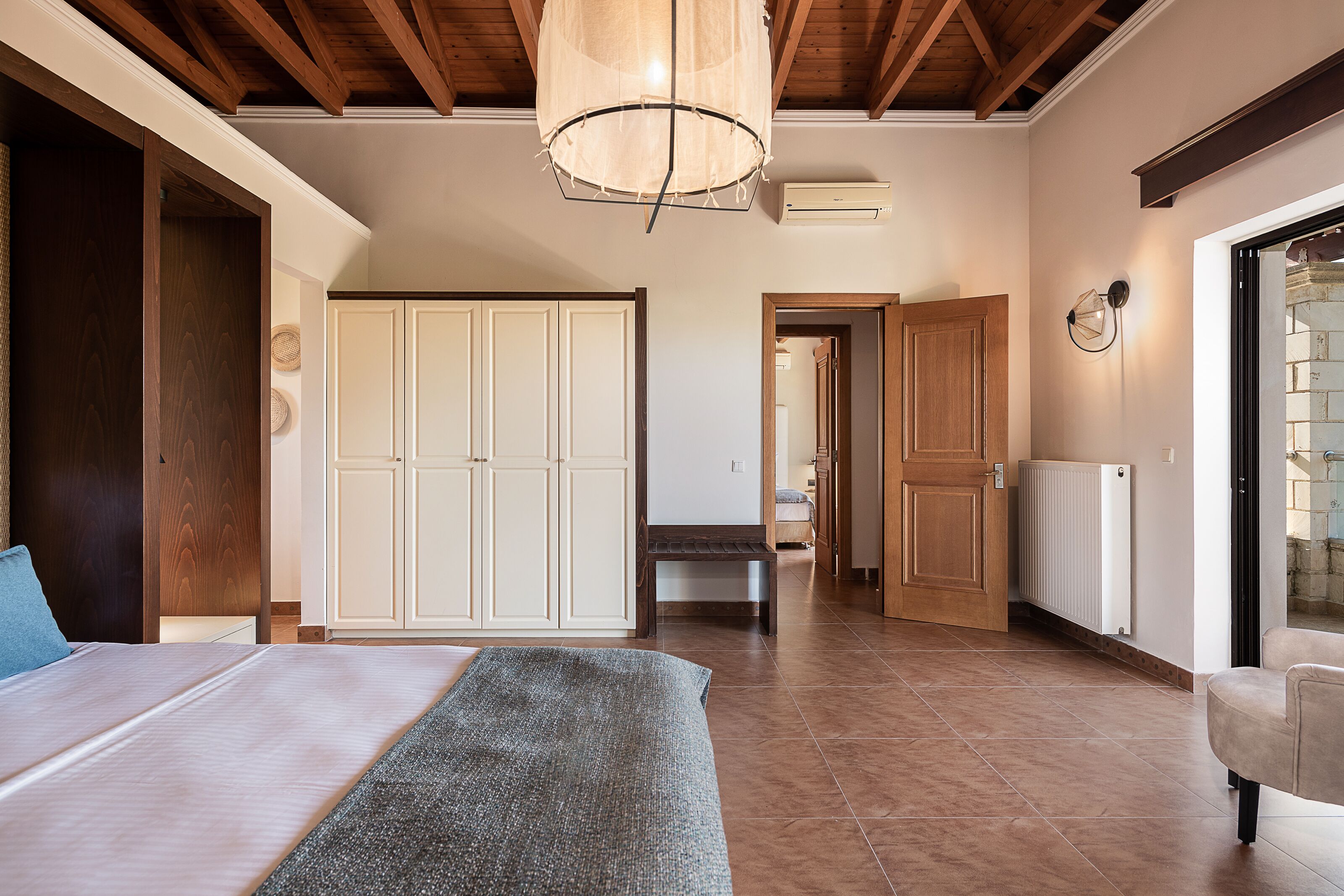 A hotel room with a bed, a bench, a wardrobe, a bench in the hallway, and a door leading to another room.