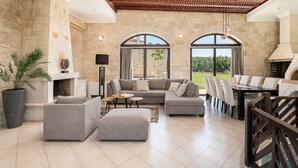 Un vaste espace de vie agrémenté d’une cheminée en pierre, d’un grand canapé d’angle et d’une table à manger avec des chaises.