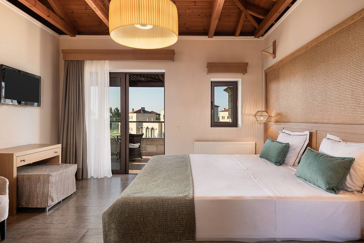 Ein Schlafzimmer mit Bett, Schreibtisch, Fernseher und Blick ins Freie.
