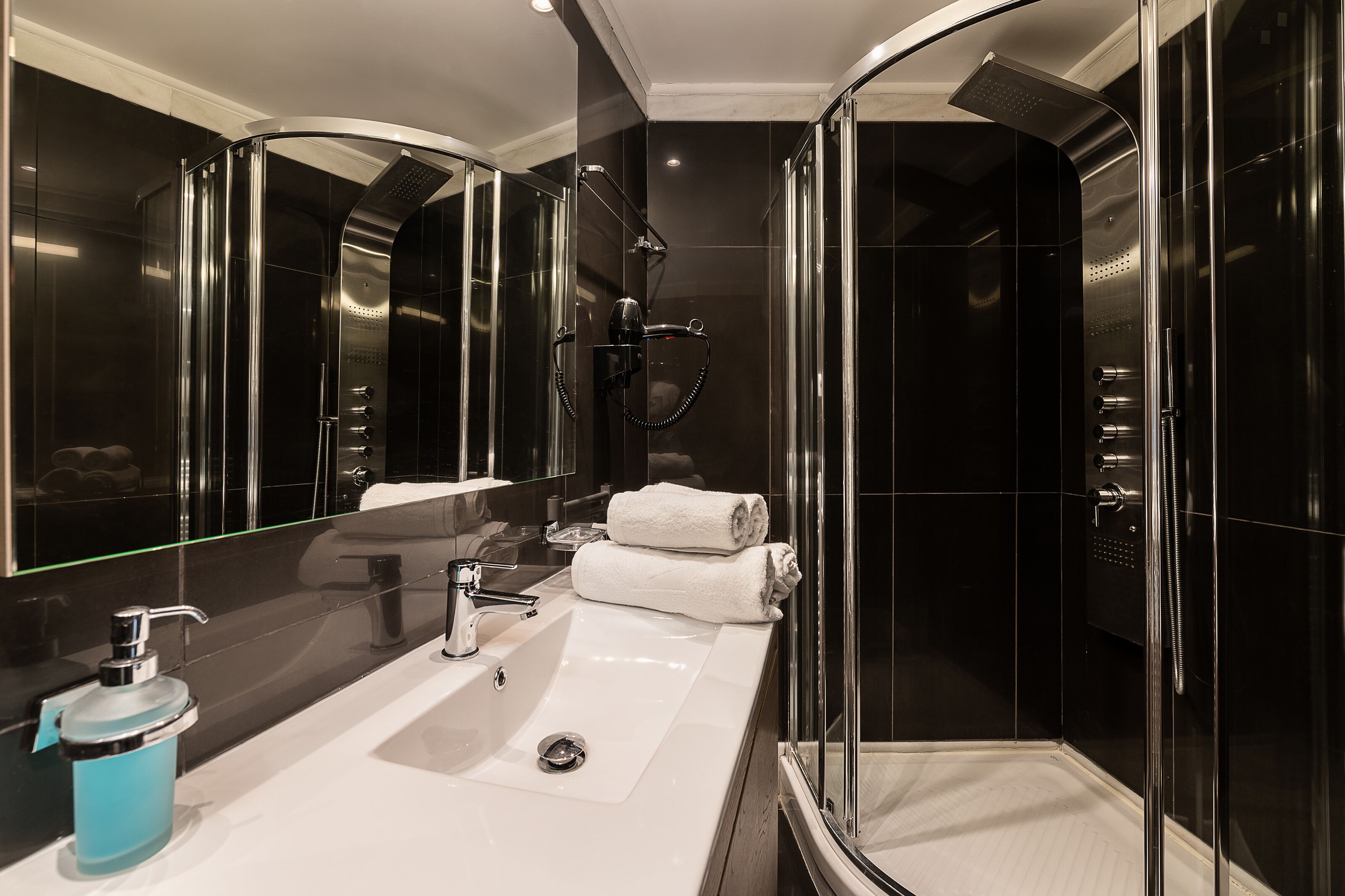 A modern bathroom with a glass-enclosed shower, a large mirror, and a white sink with a blue soap dispenser.