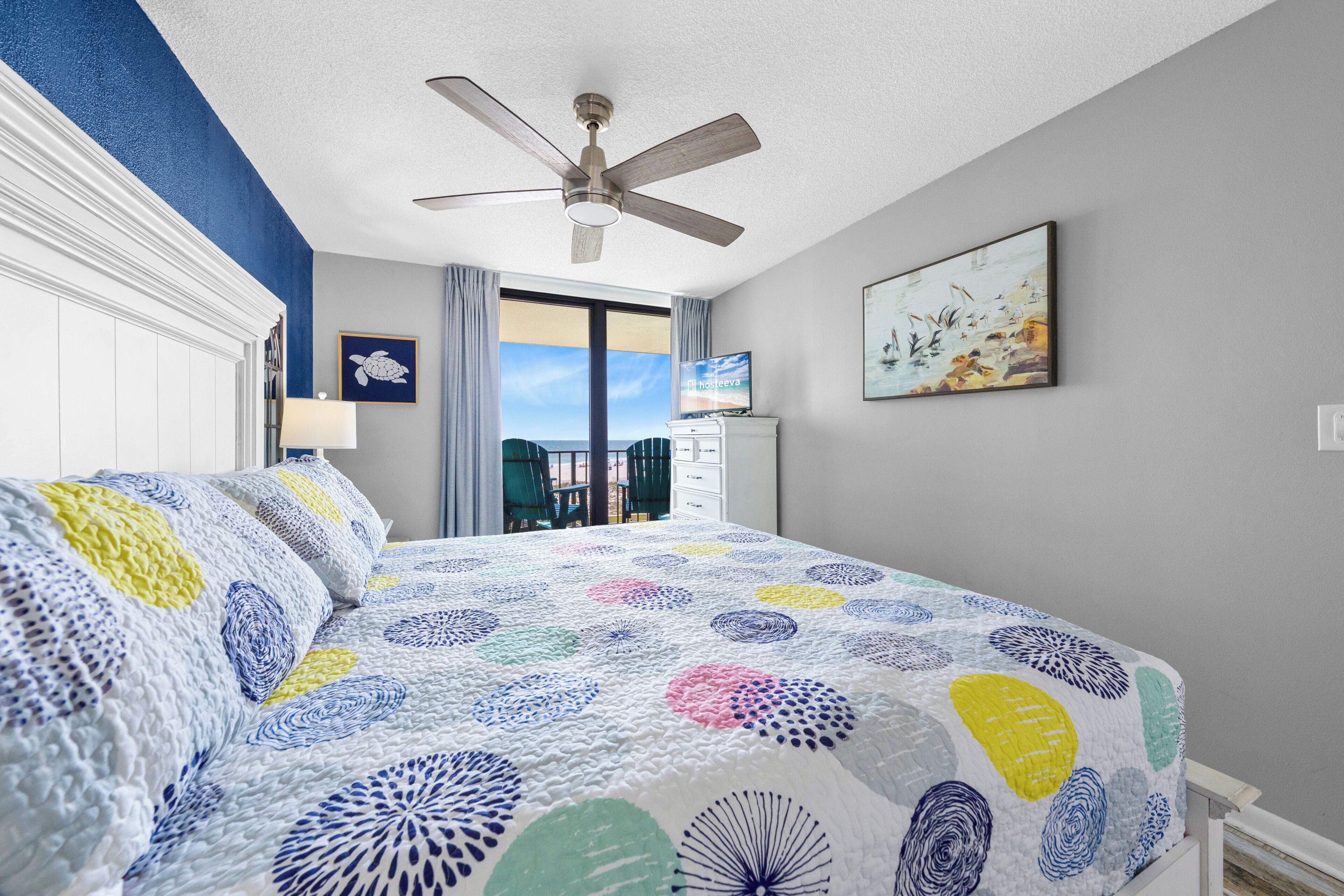 A hotel room with a bed, a ceiling fan, a television, and a view of the outdoors.