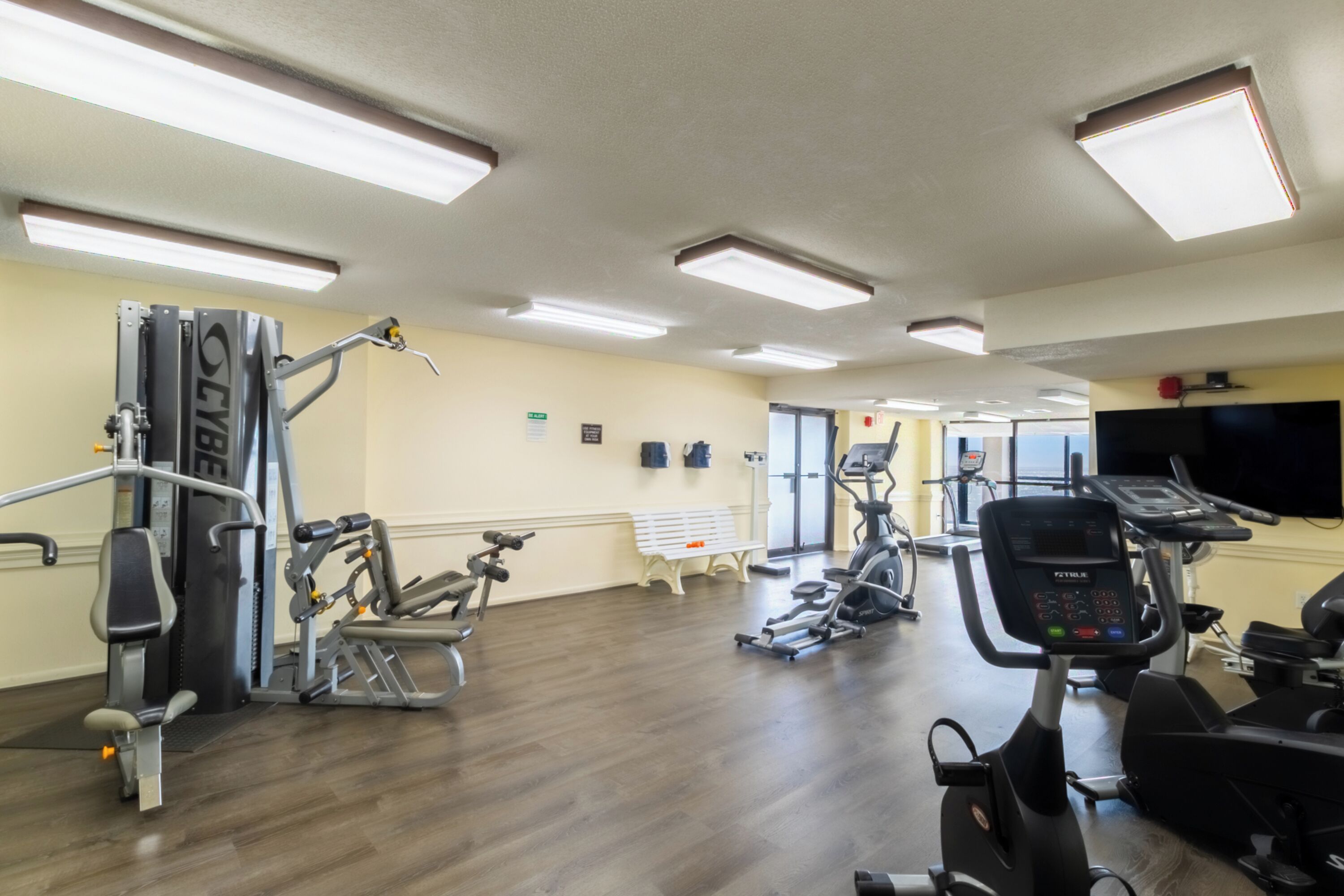 Un gimnasio con diferentes máquinas de ejercicio, una banca y una pantalla de televisión.
