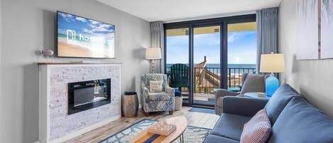 A modern living room with a fireplace, a flat-screen TV, a sofa, and a balcony with a view.