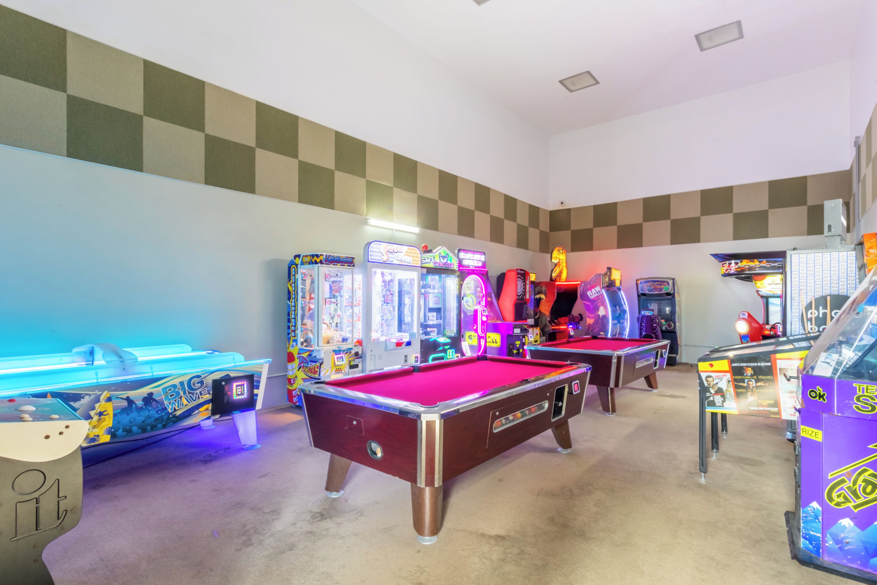 Une salle avec des tables de billard, des jeux d’arcade et un motif à carreaux sur les murs.