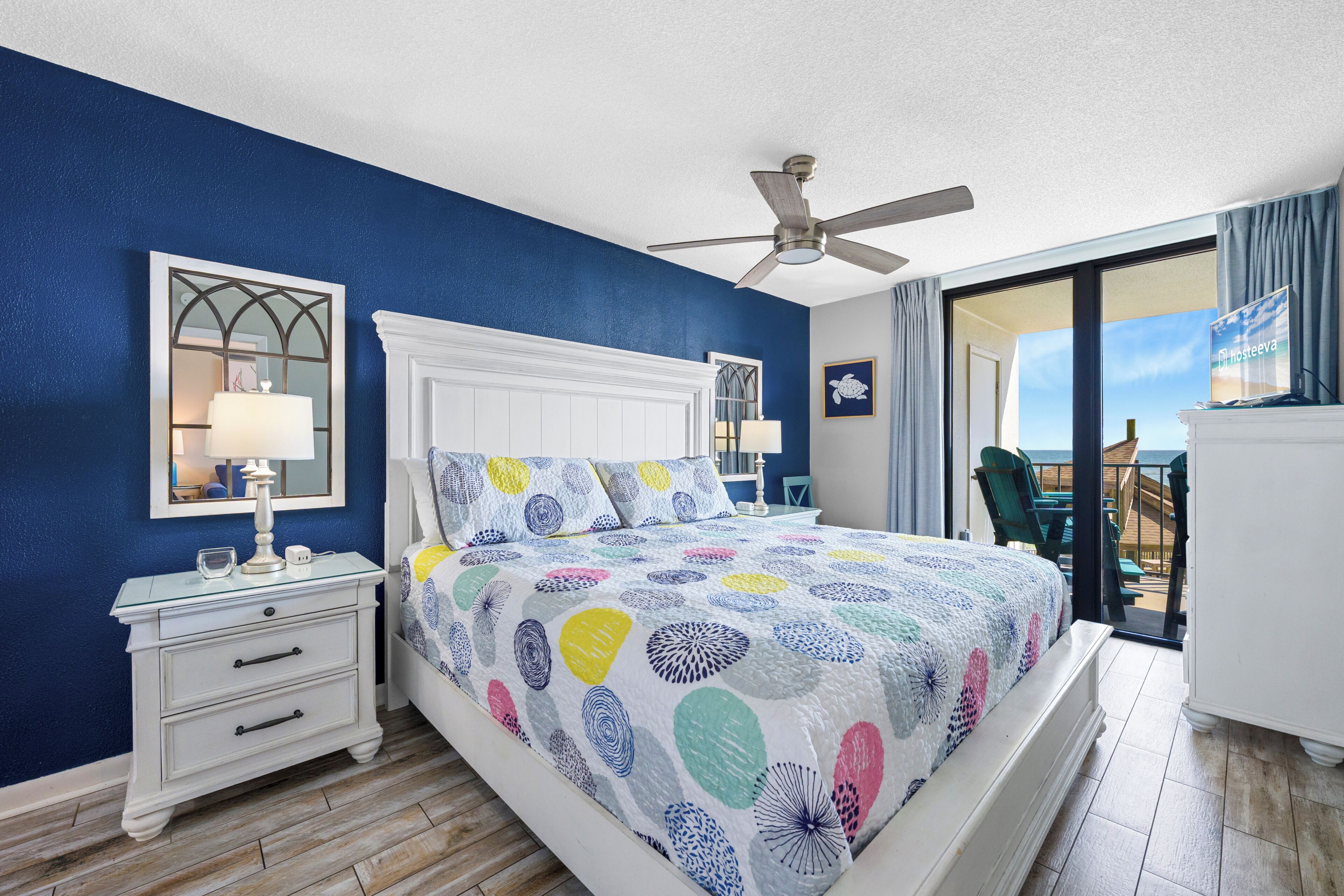 A bedroom with a bed, a nightstand, a ceiling fan, a window with a view, and a balcony.