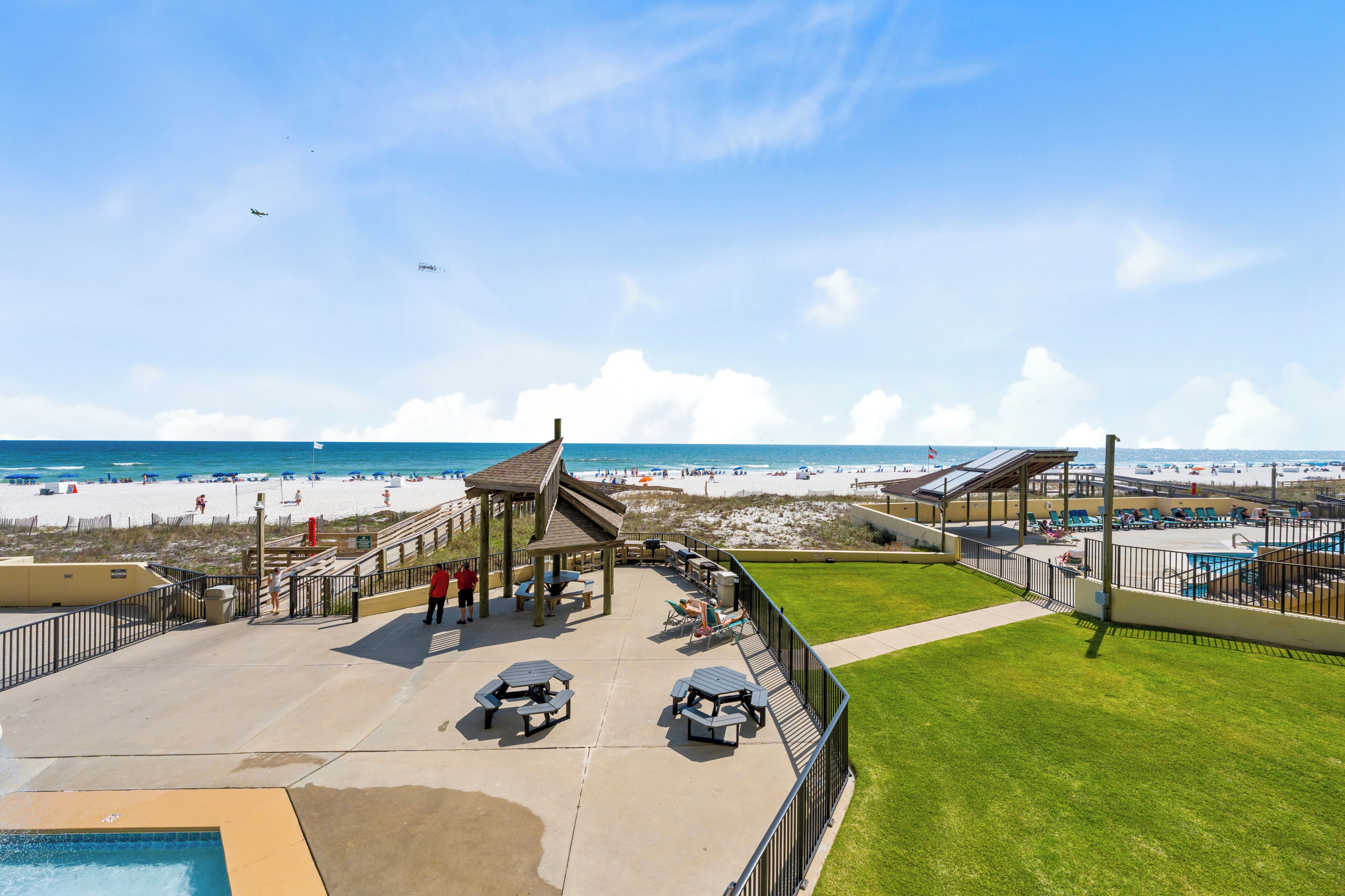 A beachside hotel patio with a pool, lounge chairs, and a gazebo overlooking the beach.
