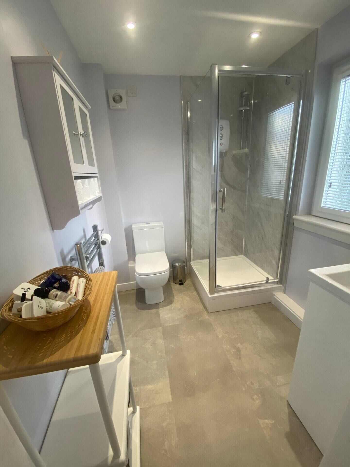 A modern bathroom with a glass-enclosed shower, a toilet, and a vanity with a basket of toiletries.