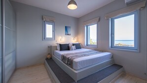A bedroom with a bed, two windows, a painting, and a ceiling light. - A private Villa infront of the sea (Paros Island)