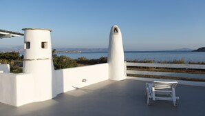 A white outdoor terrace with a white bench and a small tower structure, overlooking a body of water and distant mountains. - A private Villa infront of the sea (Paros Island)