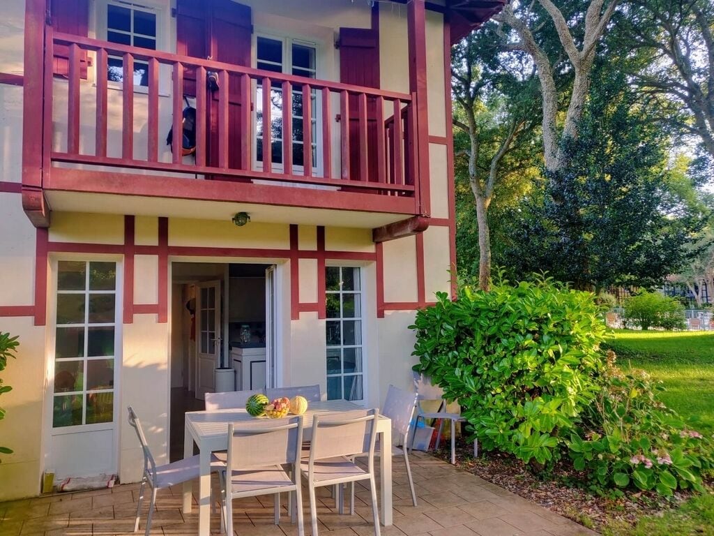 Een gebouw met twee verdiepingen, een balkon, een eethoek met stoelen en een tafel, en een verzorgde tuin.