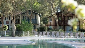 A pool area with lounge chairs and a building with a balcony in the background. - Villa ALICE ideally located in the heart of the MOLIETS-ET-MAA golf course (MOLIETS-ET-MAA)